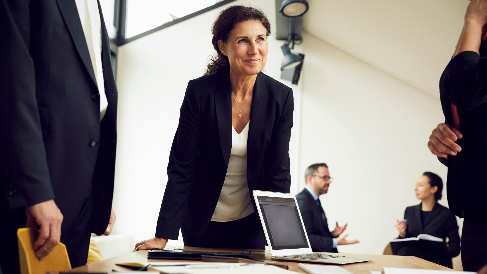Business woman smiling and leaning against a table