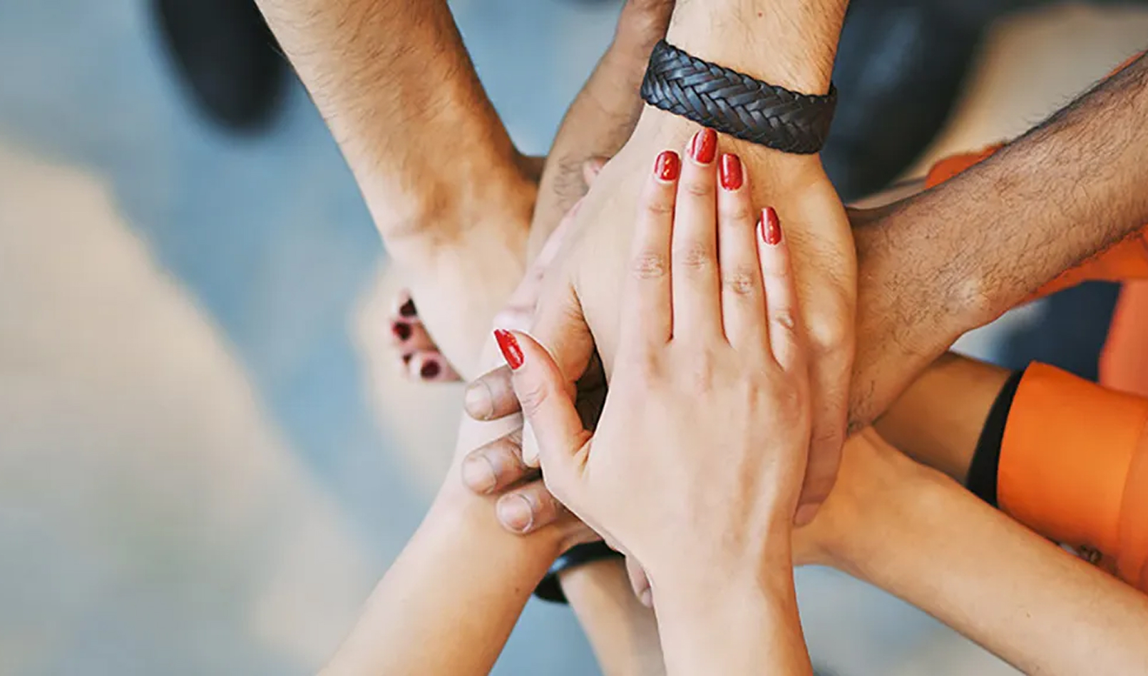 An overhead shot of several diverse hands stacked one on top of the other in a gesture of unity. The image represents the spirit of partnership and teamwork at the heart of our community involvement initiatives.