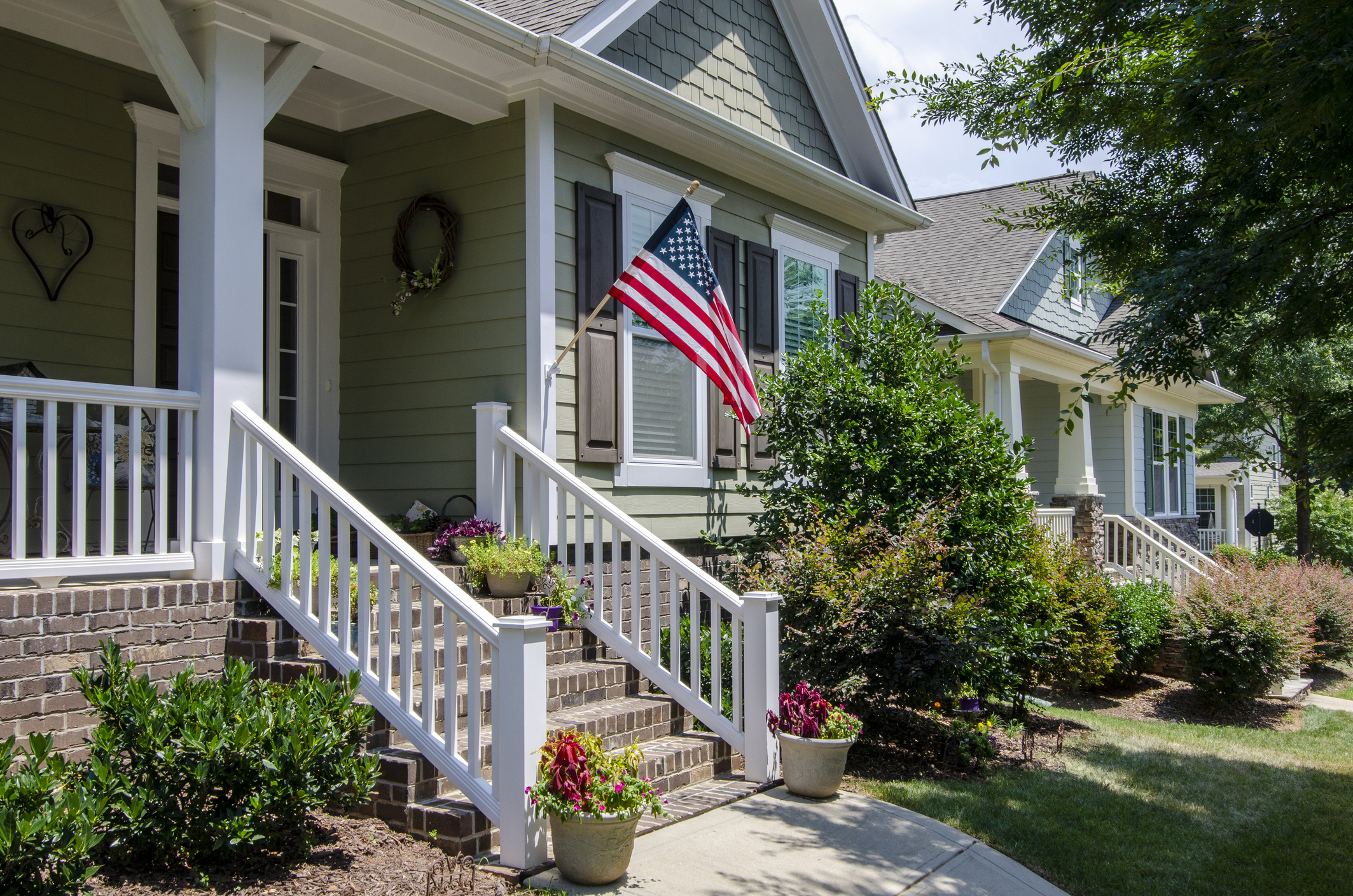 Front porch of a well-landscaped home with a mounted American flag