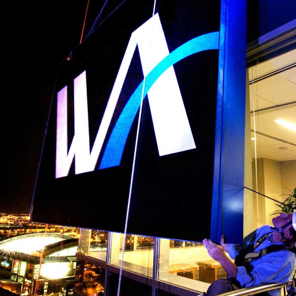Two men hanging a large sign at the top of a skyscraper