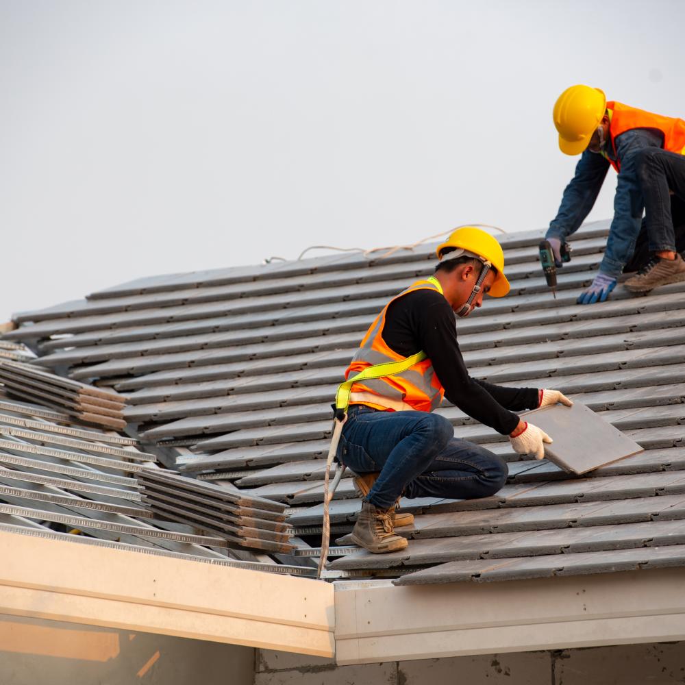 Two roofers in orange vests re-shingling a house roof.