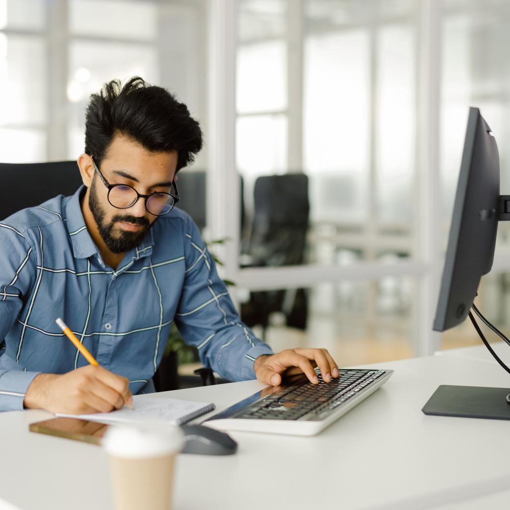 A young man working dilligently at a computer desk. He respresents the peace of mind gained from Positive Pay protections.